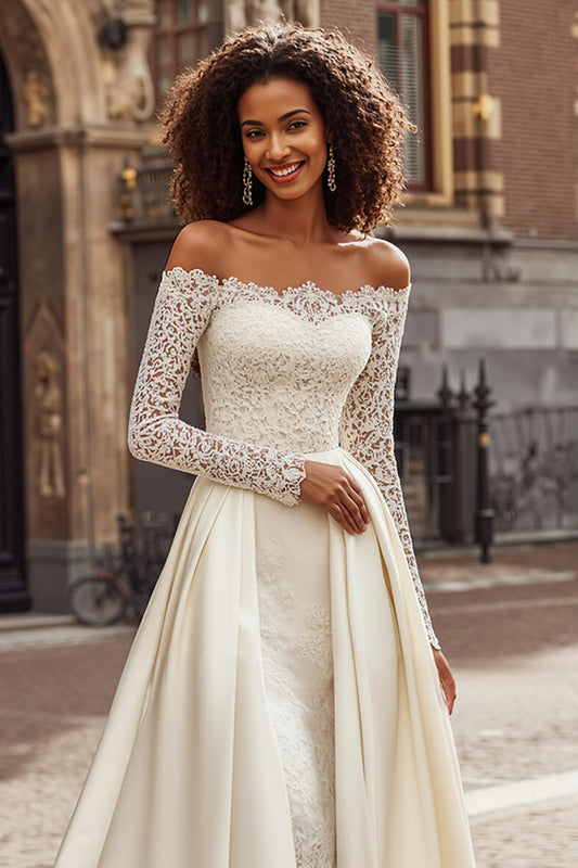 Robe de mariée trapèze ivoire, épaules dénudées, avec des appliques de dentelle et une traîne.