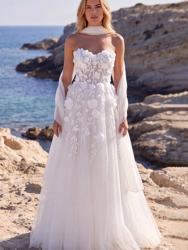 Robe de mariée longue blanche en tulle coupe évasée, ornée de fleurs, corsage cœur et appliqués